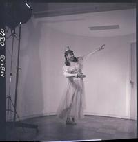 [Bailarina de ballet, caracterizada para una obra, posando de pié en una posición de movimiento]