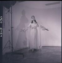 [Bailarina de ballet, caracterizada para una obra, posando de pié con los brazos extendidos]