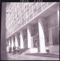 [Dos señoras acompañadas de un caballero, en el frontis de un gran edificio]