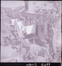 [Tres niños pequeños y una mujer que tiende ropa junto a su vivienda en un sector popular]