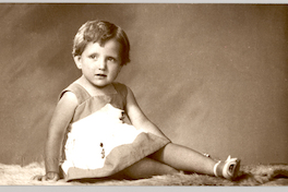 [Niñita rubia sentada de lado con las piernas cruzadas, vestido de dos colores y chalas blancas]