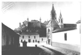 [Iglesia del Carmen, al costado de una calle, y de fondo se divisa una construcción en un cerro]