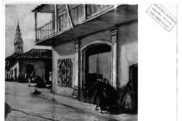 [Casa esquina de la colonial, junto a una calle. Por la vereda camina una pareja, y de fondo está la torre de una iglesia]