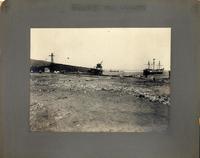 [Vista del muelle desde la playa, se divisan gruas y un barco]