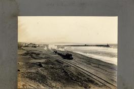 [Vista de una locomotora de carga, pasando por la orilla del mar]