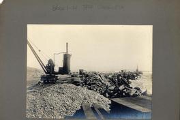 [Vista del terminal marítimo, con unas maquinarias como grúas, parte de vías férreas, rodeado por el mar]