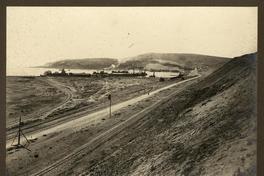 [Vista panorámica del puerto, desde el cerro, se divisa el muelle, almacenes, vías férreas y unos barcos en el mar]