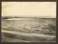 [Vista de una vía férrea, en sector costero, se divida una poza de mar, y de fondo el muelle]