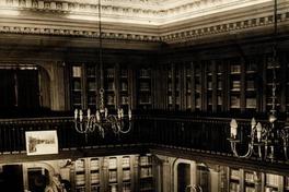 [Vista interior de la Biblioteca Americana Barros Arana, Sala Medina, Biblioteca Nacional: espacio revestido en madera de nogal, Anaqueles con puerta de vidrio, parquet de maderas nobles, lámparas de techo en bronce, de 8 brazos con bombillas como velas, balconada en el segundo piso, busto de Barros Arana]