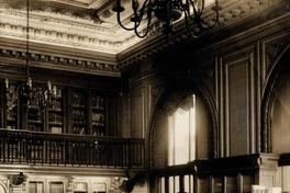[Vista interior del fondo Bibliográfico Sala Medina, Biblioteca Nacional: Espacio revestido en madera de nogal, Anaqueles con puerta de vidrio, parquet de madera noble, lámparas de techo en bronce, de 8 brazos con bombillas como velas, balconada en el segundo piso, mobiliario de maderas nobles]