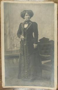 [Mujer joven vestida con un conjunto de terciopelo, vestido y chaqueta larga, blusa de cuello alto, luce joyas]