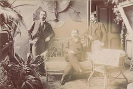 [Hombre sentado con dos personas de pie a sus costados]