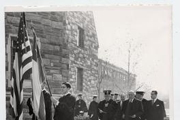 [Guillermo Feliú Cruz junto a otros señores en ceremonia de graduación, caminando por costado de edificio, detrás de los estandartes chileno y norteamericano. Estados Unidos]