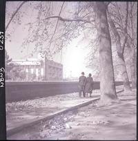 [Una pareja paseando por el Parque Forestal, en la ladera opuesta del río Mapocho, la Escuela de Derecho de la Universidad de Chile]