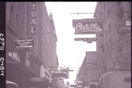 Calle Huérfanos, con sus avisos luminosos de casas comerciales, como la Marquesina Cine Central, Café Santos, Peluquería Confort para Caballeros, Instituto de Belleza Berthe, etc. y autos estacionados en ambos costados