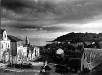 Calle Lota, al costado izquierdo, se aprecia la torre de la Iglesia del Colegio María Auxiliadora, construida en 1915; al fondo, se observa la Bahía de Puerto Montt y la Isla Tenglo