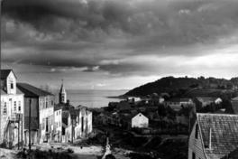 Calle Lota, al costado izquierdo, se aprecia la torre de la Iglesia del Colegio María Auxiliadora, construida en 1915; al fondo, se observa la Bahía de Puerto Montt y la Isla Tenglo