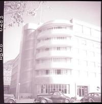 [Autos estacionados en el frontis de un edificio, atrás se divisa un cerro]