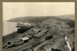 [Vista panorámica del puerto, se divisa el muelle, terminal ferroviario con una locomotora, vías férreas y almacenes]