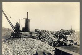 [Vista del terminal marítimo, con unas maquinarias como grúas, parte de vías férreas, rodeado por el mar]