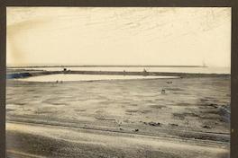 [Vista de una vía férrea, en sector costero, se divida una poza de mar, y de fondo el muelle]