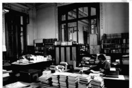[Biblioteca Nacional, vista general de la oficina catalogación, con dos personas trabajando]